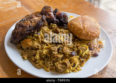 Jamaican food.  Traditional Jamaican curried goat, jerk chicken and fried dumpling with rice and peas. Stock Photo