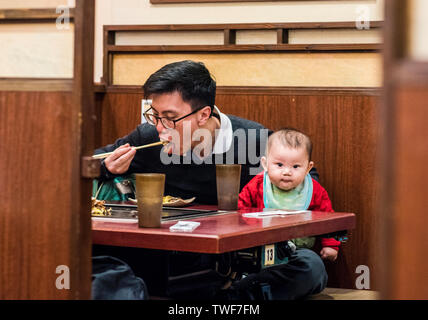 Man sitting in restaurant eating lunch with toddler sitting beside him in the Ponto-cho area of Kyoto in Japan. Stock Photo