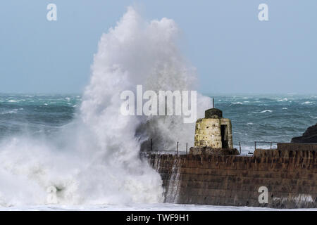 Wild weather battering the Cornish coast with a huge powerful wave breaking over the historic Monkey Hut on the pier at Portreath in Cornwall. Stock Photo