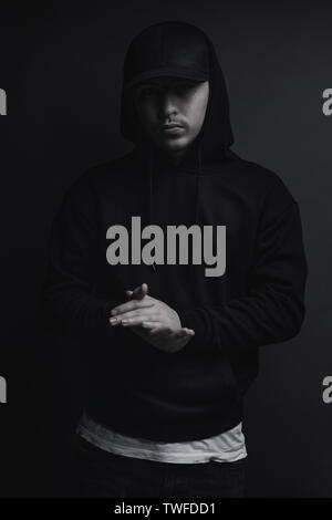 young cool rapper with black hoodie and cap clap his hands in front of grey background Stock Photo