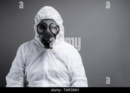 man with gas mask in protective overall suit against grey background