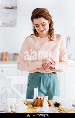 Smiling curly woman looking at easter cake on table Stock Photo