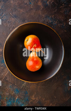 Fresh red-yellow pears on a plate on brown table, top view Stock Photo