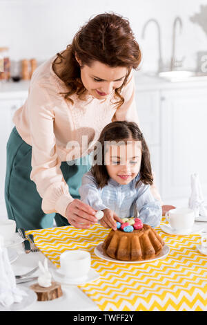 Mother and daughter decorating easter cake with painted eggs in kitchen Stock Photo
