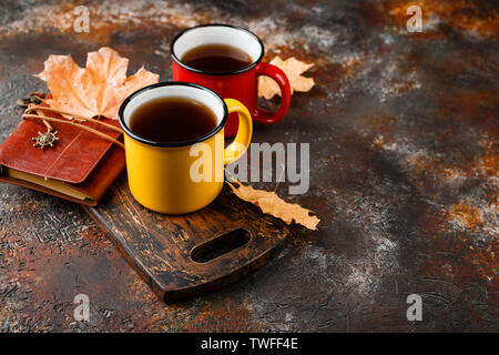 Two colored enamel tea cups, autumn maple leaves on rusty brown background Stock Photo