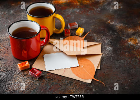 Two colored enamel cups of tea, two envelops, watercolors in cuvettes, , autumn leaves and bumps on a rusty brown background Stock Photo