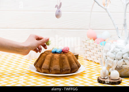Cropped view of woman putting painted quail egg on easter cake in kitchen Stock Photo