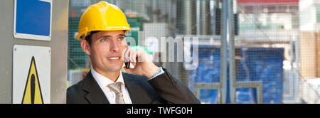 Panorama of man male builder foreman, construction worker, site manager engineer or surveyor on building site wearing a hard hat talking on a mobile c Stock Photo