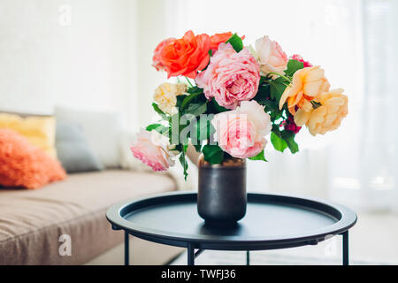 Interior of living room decorated with flowers on coffee table and cozy couch with cushions. Bouquet of colorful fresh roses Stock Photo