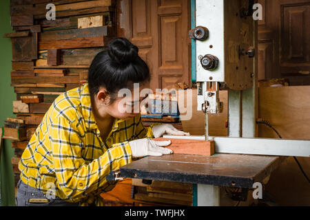 Women standing is craft working cut wood at a work bench with band saws power tools at carpenter machine in the workshop Stock Photo