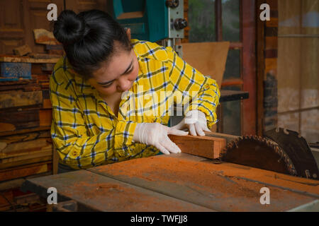 Women standing is craft working cut wood at a work bench with band saws power tools at carpenter machine in the workshop Stock Photo