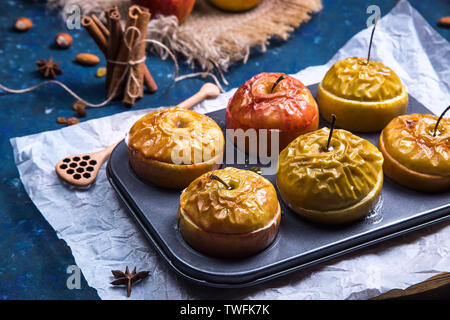 Baked apples stuffed with nuts, raisins with honey and cinnamon on a blue background among the ingredients for cooking. Autumn healthy dessert Stock Photo