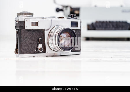 Old film camera on white plank background. Typewriter on the background. Vintage photo. Stock Photo