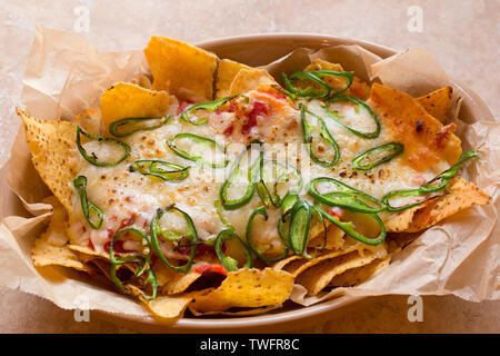 A homemade dish of nachos which contains tortilla chips, hot salsa, grated cheddar cheese and sliced green chillis that have been cooked under a grill Stock Photo