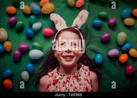 Overhead portrait of young girl wearing bunny ears surrounded by Easter eggs Stock Photo