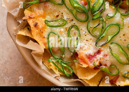 A homemade dish of nachos which contains tortilla chips, hot salsa, grated cheddar cheese and sliced green chillis that have been cooked under a grill Stock Photo