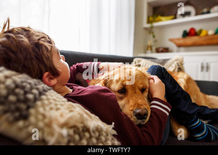 Boy lying on a couch cuddling a golden retriever dog Stock Photo