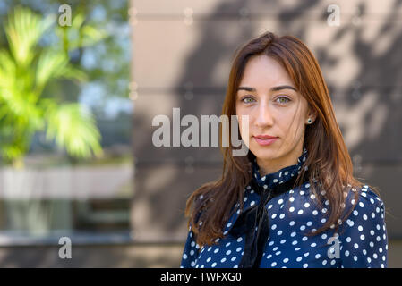 Serious thoughtful young woman posing outdoors in the shade of a tree looking at the camera with a speculative expression and copy space Stock Photo