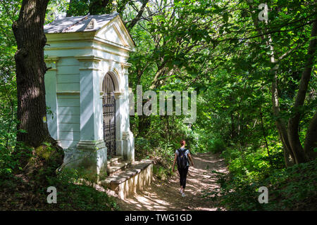 One cabin of the Stations of the Cross along forest trail and a young woman walking past in Kőszeg, Hungary Stock Photo