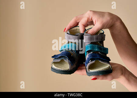 Female is holding close-up a special children's orthopedic shoe sandals made of genuine leather. Comfortable shoes isolated on light background with c Stock Photo