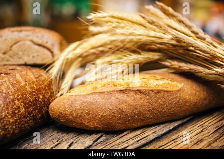 Assortment of baked various whole grain breads and wheat ear or spike on wooden table. Stock Photo
