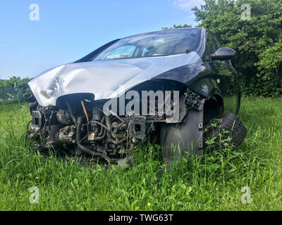 The wreck of the car is standing on the grass with broken wheel and without the front parts. Maybe after the frontal crash.