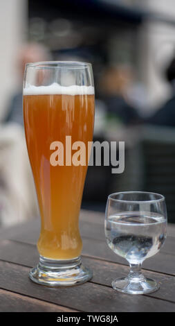 Wheat beer on table full pint served with half full glass of mineral water on wooden table outside setting, viewed from the side Stock Photo