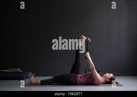 Young Woman Using Yoga Belt While Doing Exercise On Fitness Mat At