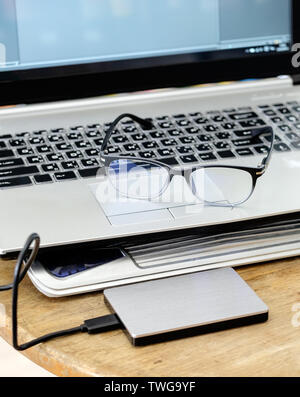 Notebook grey modern black keyboard with hdd grey and spectacles on wood table Stock Photo