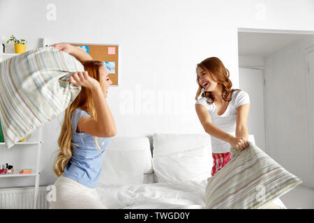 happy teen girl friends fighting pillows at home Stock Photo