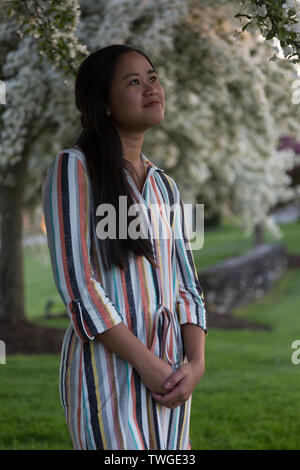 A beautiful teenage girl looks up at the flowering trees in Fort Wayne, Indiana, USA. Stock Photo