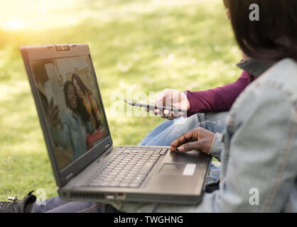 couple of multi-ethnic girls student sitting on meadow at notebook Stock Photo