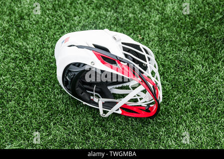 A red and white high school lacrosse helmet left on a green turf field. Stock Photo