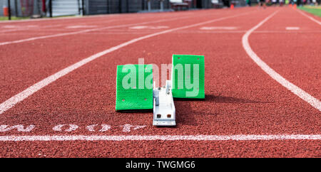 A set of green starting blocks are ready for a sprinter to run the 400 meter dash on a red track. Stock Photo