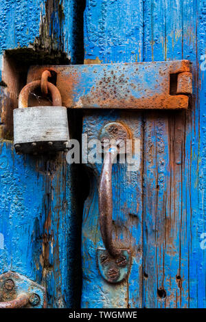 Padlock and clasp with rust on cracked and peeling blue door Stock Photo