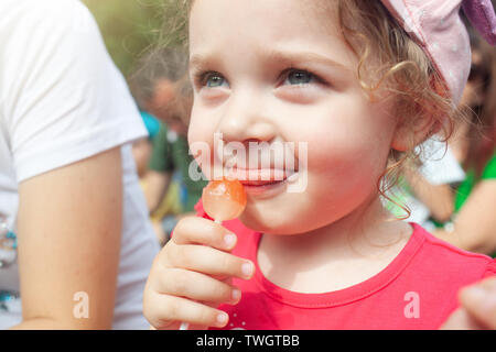 Cute little girl holding in hand a cherry lollipop. Stock Photo