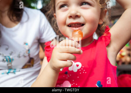 Cute little girl holding in hand a cherry lollipop. Stock Photo