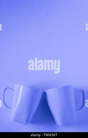 2 monochromatic blue coffee mugs on blue background clinking in cheers with blank empty room space for text, copy, or copyspace. Modern top view conce Stock Photo