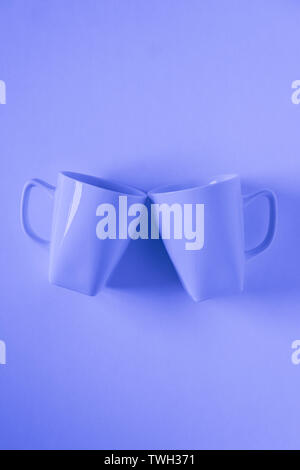 2 monochromatic blue coffee mugs on blue background clinking in cheers with blank empty room space for text, copy, or copyspace. Modern top view conce Stock Photo