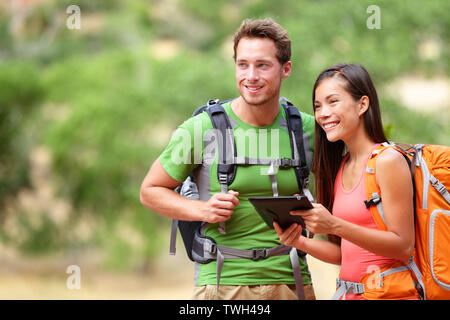 Tablet computer - couple hiking using internet and tablet computer pc guide book app on hike in Zion National Park. Interracial active hiker couple, Asian woman, caucasian man trekking in Utah, USA.