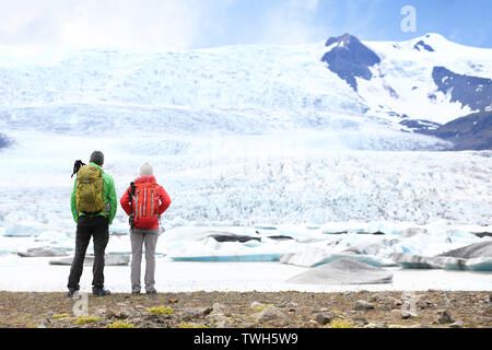 Hiking adventure travel people on Iceland. Hikers looking at glacier and glacial lagoon / lake of Fjallsarlon, Vatna glacier, Vatnajokull National Park. Couple visiting Icelandic nature landscape. Stock Photo