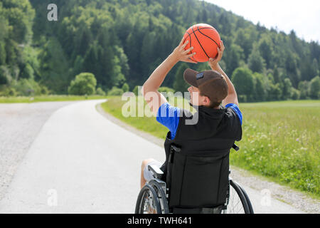 Disabled young basketball player on a wheelchair holding ball and beeing active in sport Stock Photo