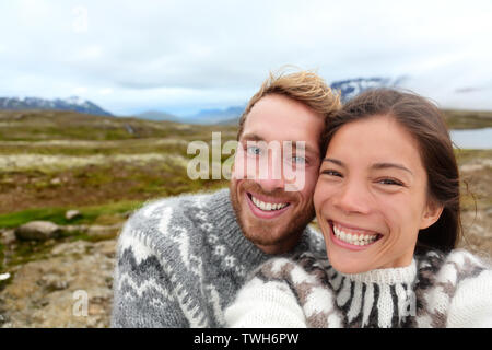 Iceland couple selfie wearing Icelandic sweaters in beautiful nature landscape on Iceland. Woman and man model in typical Icelandic sweater. Multiracial couple, Asian woman, Caucasian man. Stock Photo