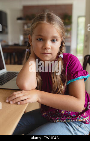 Cute girl looking at camera while sitting on dining table in a comfortable home Stock Photo