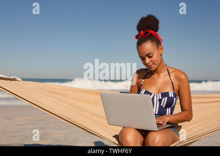 Beautiful woman using laptop on hammock at beach in the sunshine Stock Photo
