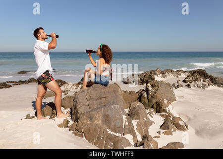 Young couple drinking beer on beach in the sunshine Stock Photo