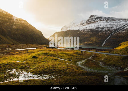 Saksun church / Saksunar kirkja as spotted in early spring before sunset with light rays, snow-covered mountains and low hanging fog (Faroe Islands) Stock Photo