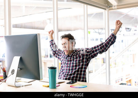 Male graphic designer celebrating success at desk in a modern office Stock Photo