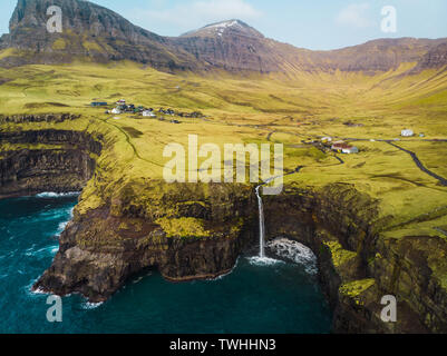 Aerial view of famous Gasadalur waterfall from above during a sunny spring day with snow-covered mountain peaks and dark blue sea (Faroe Islands) Stock Photo