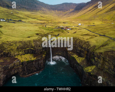 Aerial view of famous Gasadalur waterfall from above during a sunny spring day with snow-covered mountain peaks and dark blue sea (Faroe Islands) Stock Photo
